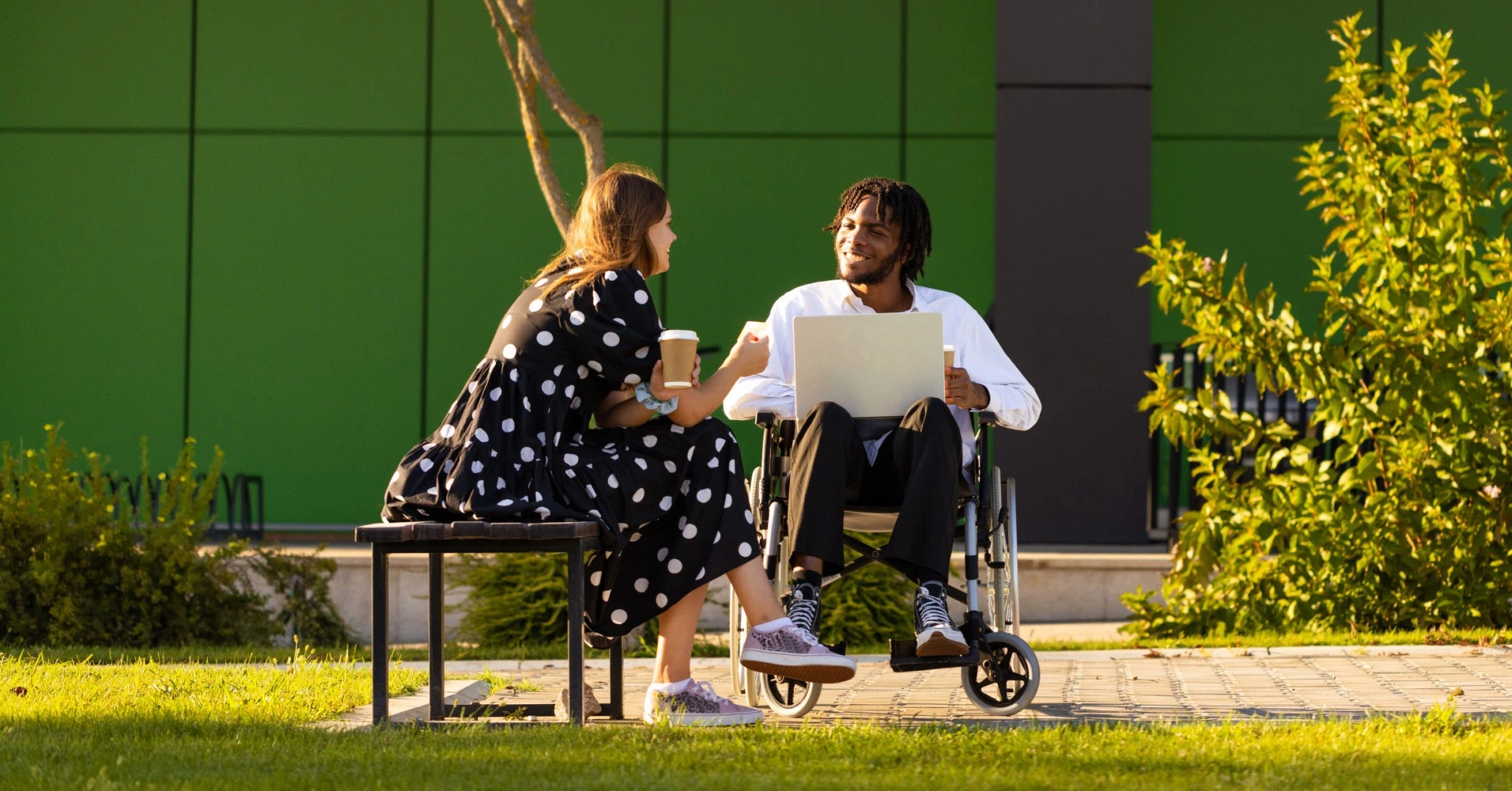 Photo of two people, one in a wheelchair holding a laptop, talking outside